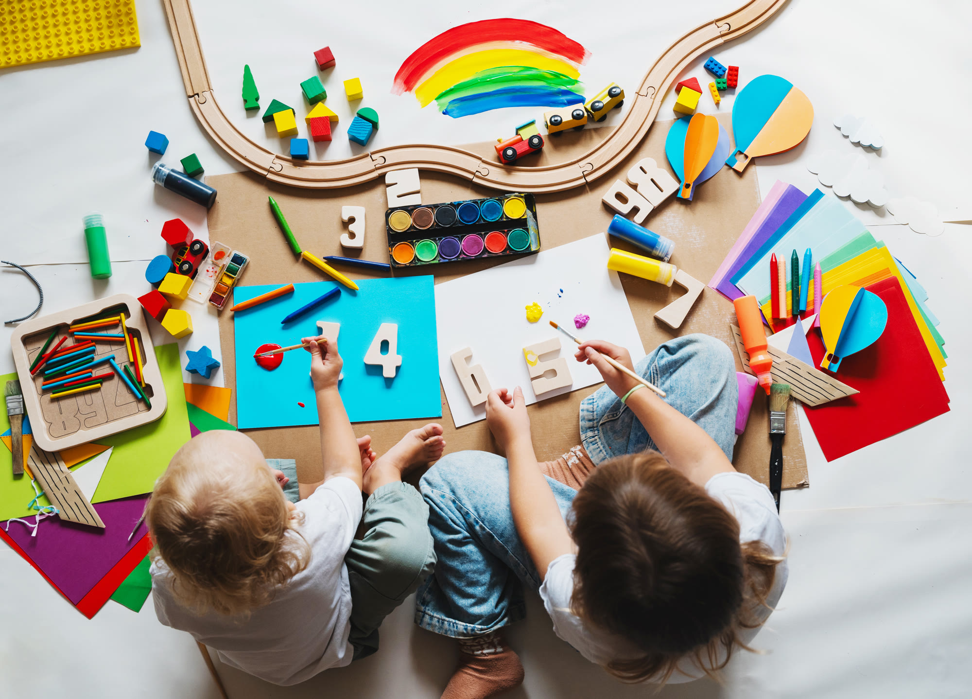 Two children painting and crafting on the floor, seen from above