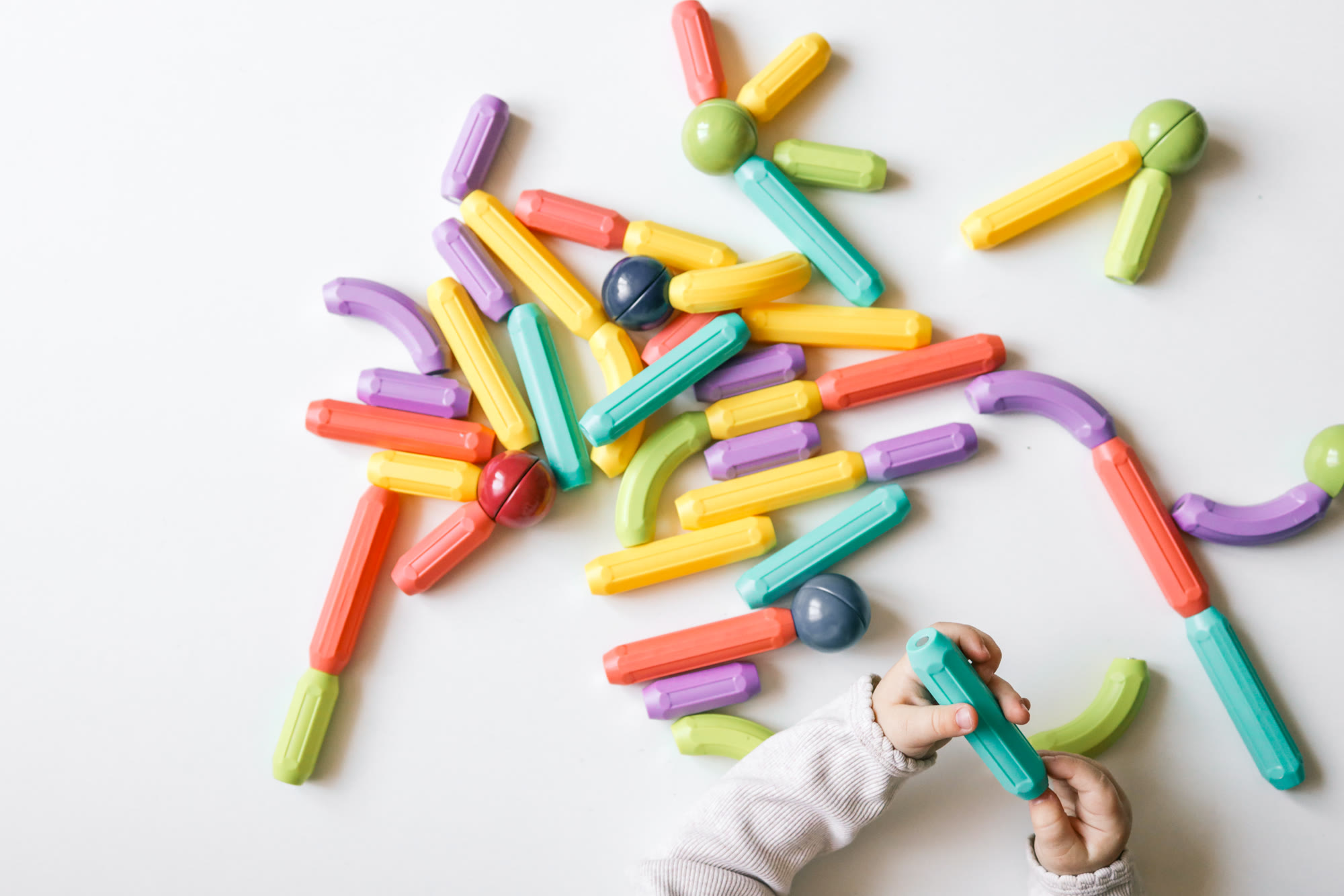 A toddler&rsquo;s hands building with colorful magnetic sticks, seen from above